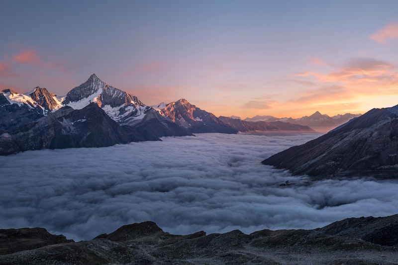 Snow-capped mountain peaks rising above a valley filled with white clouds at sunrise